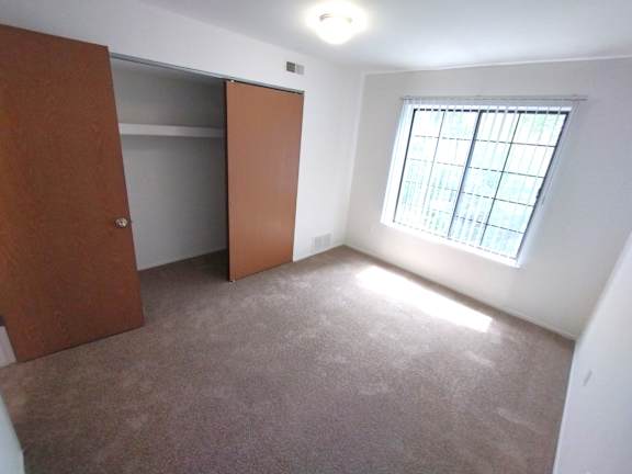 Empty carpeted bedroom with sliding closet and window at Charter Oaks Apartments, Davison, Michigan