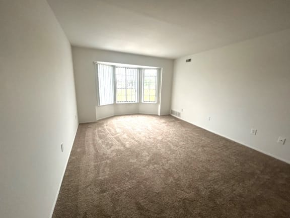 Bright living room with large bay windows at Charter Oaks Apartments, Davison, MI