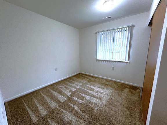 A bedroom with a carpet and a window with blinds.