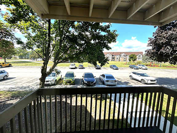 A view from a balcony looking out at a parking lot with cars and trees.