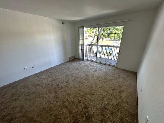 A living room with carpeted floor and a sliding glass door.