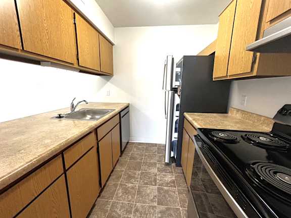 Galley kitchen with electric range and stainless refrigerator at Charter Oaks Apartments, Davison, Michigan