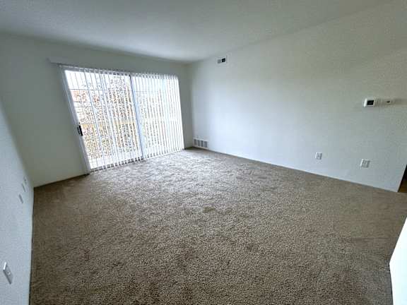 Empty carpeted room with sliding glass door and vertical blinds at Charter Oaks Apartments, Michigan, 48423