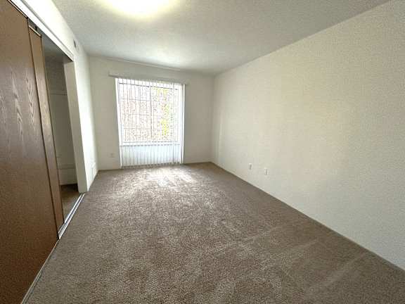 Bright carpeted bedroom with mirrored closet and window at Charter Oaks Apartments, Michigan, 48423