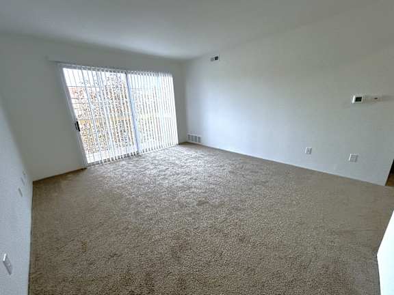 Bright carpeted living room with sliding glass door at Charter Oaks Apartments, Michigan, 48423