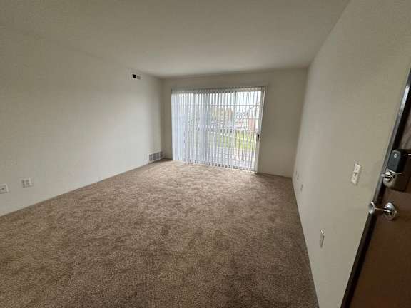 A living room with a carpeted floor and a window with blinds.