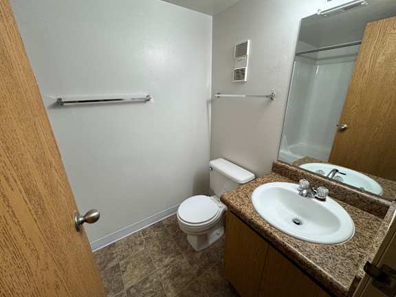 A bathroom with a toilet, sink, mirror, and shower.