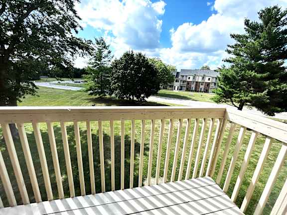A wooden deck overlooks a grassy area with trees and a building in the distance.