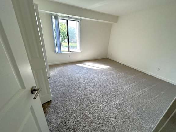 A bedroom with a carpeted floor and a window letting in natural light.
