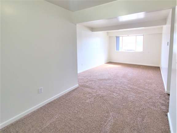 A dining room and living room with a carpeted floor and a window.