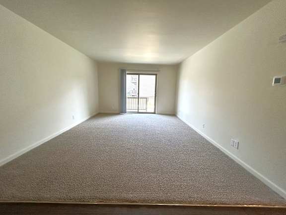 A carpeted  living room with a door leading to a balcony.