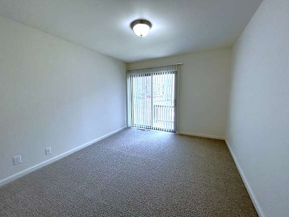 A bedroom with a carpeted floor and a window with blinds.