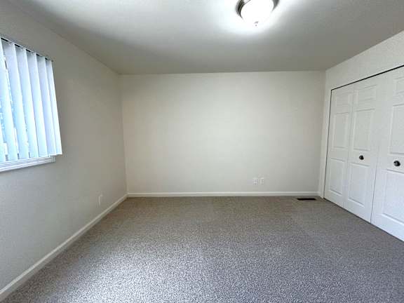 A white bedroom with a carpeted floor and a window with blinds.