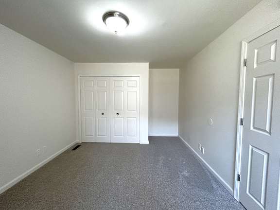 A bedroom with a grey carpet and closet.