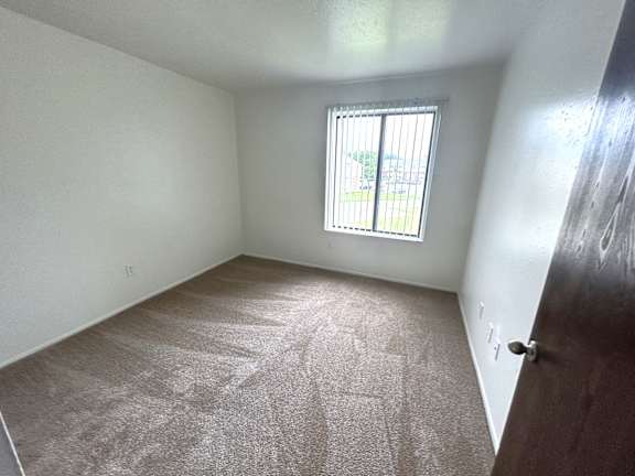 A bedroom with a carpeted floor and a window with bars on it.