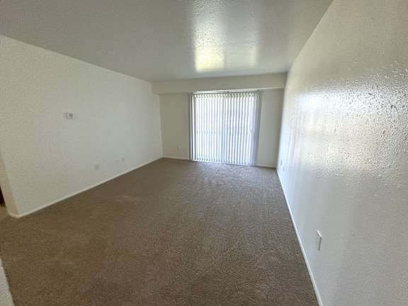 A living room with a carpeted floor and a window with blinds.