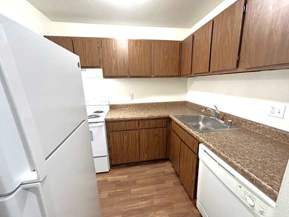 A kitchen with a white refrigerator, brown cabinets, and a white dishwasher.