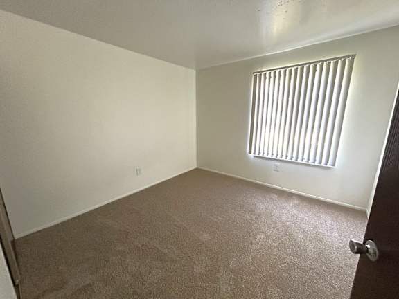 A bedroom with a carpeted floor and a window with blinds.
