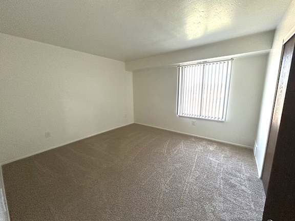 A bedroom with a carpeted floor and a window with blinds.