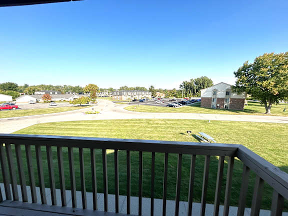 A view from a balcony overlooking a grassy area with a building in the distance.