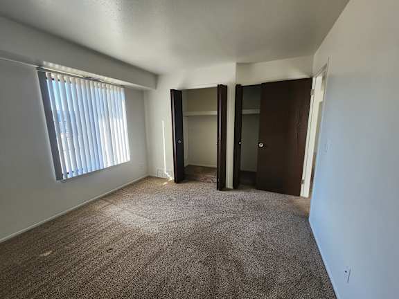 A bedroom with a carpeted floor and a window with blinds.