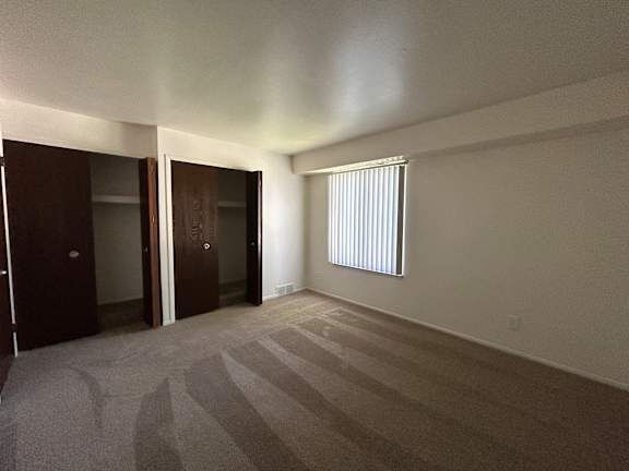 A bedroom with carpeted floor and a window with blinds.