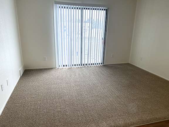 Empty carpeted room with sliding glass door and blinds at Huntington Place Apartments, Essexville, MI