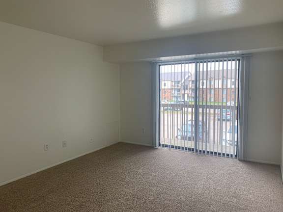 A living room with a carpeted floor and a sliding glass door.