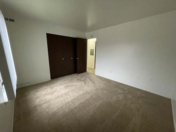 A bedroom with a carpeted floor and two brown doors.