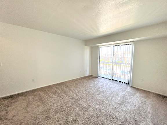 A living room with a carpeted floor and a window with blinds.