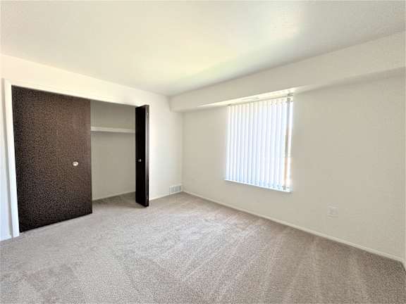 A bedroom with a brown door, a window with blinds, and a carpeted floor.