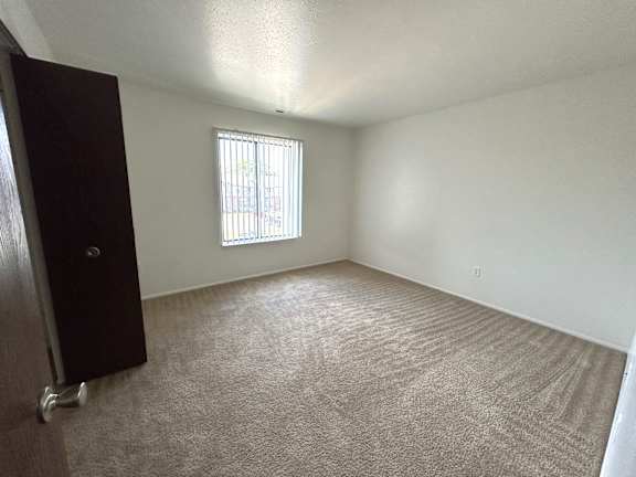 A bedroom with a carpeted floor and a window with blinds.