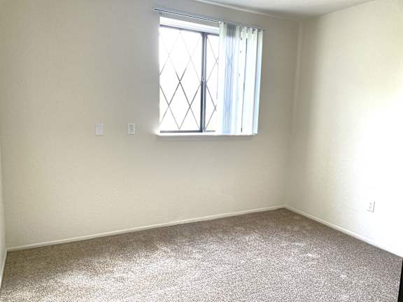 A bedroom with a carpeted floor and a window with a white curtain.