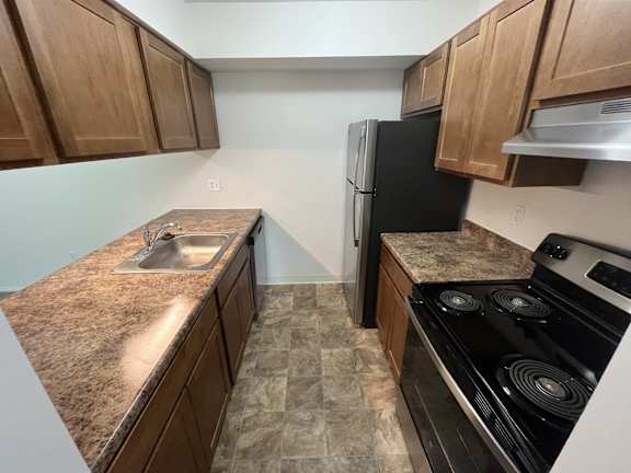 A kitchen with a black refrigerator and a stove top oven.