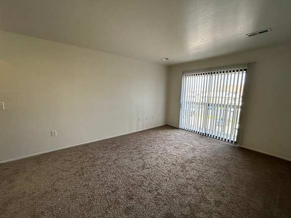 A living room with a carpeted floor and a window with blinds.