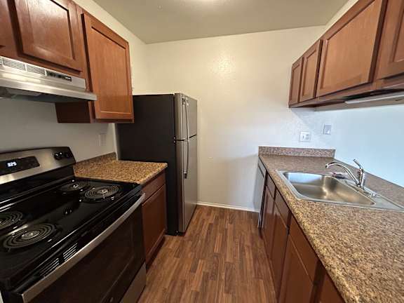 A kitchen with a black stove top oven, a black refrigerator, and brown cabinets.