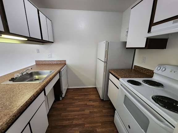 A kitchen with a white stove, refrigerator, and dishwasher,  and white cabinets.