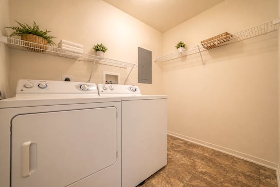 A white washing machine in a laundry room with shelves above it.