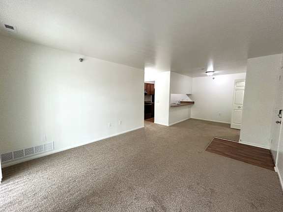 A spacious living room and dining room with a carpeted floor and a ceiling fan.