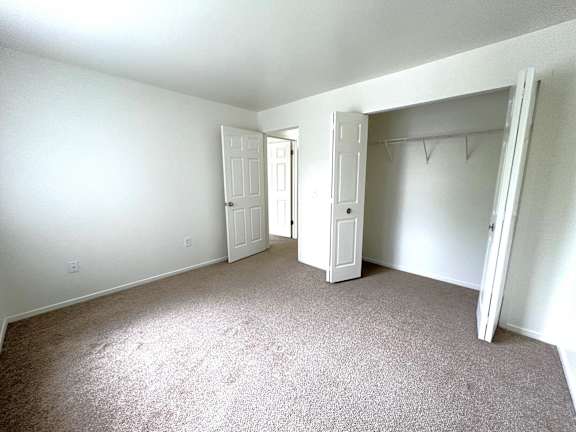 A bedroom with carpeted floor and white walls with a doorway leading to another room.