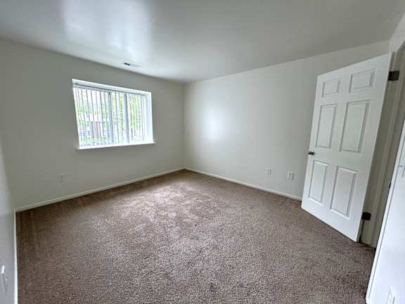 A bedroom with a carpeted floor and a window with blinds.