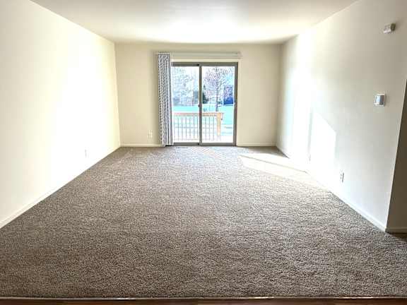 A living room with a carpeted floor and a sliding glass door leading to a balcony.