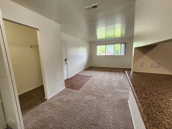 A dining room and living room with a carpeted floor and a window.