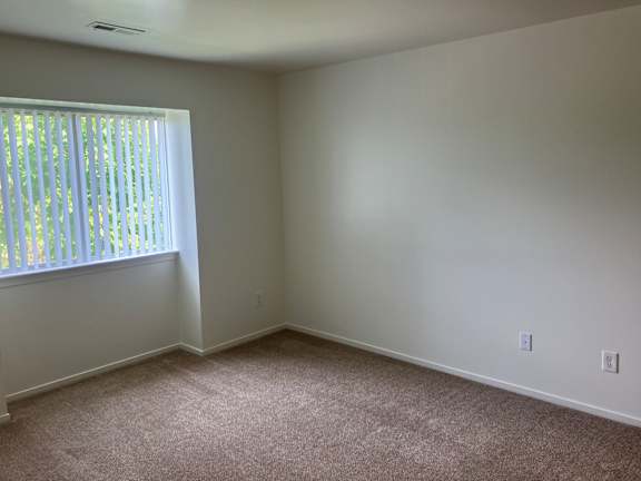 A  bedroom with a window and carpeted floor.