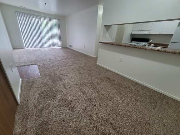 A living room and dining room with a carpeted floor and a window with blinds.