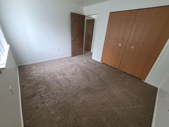 A bedroom with brown carpet and two brown doors.