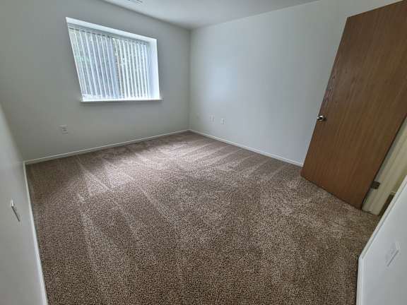 A bedroom with a brown carpet and a wooden door.