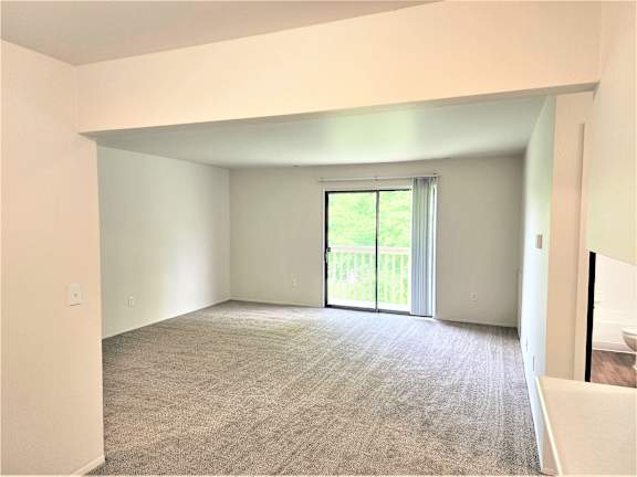 A living room with a carpeted floor and a sliding glass door leading to a balcony.