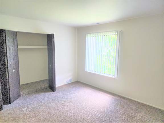 A bedroom with a carpeted floor, a window with blinds, and a door.