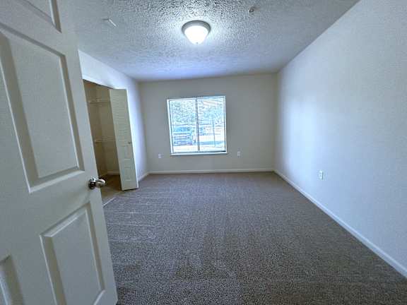 Vacant carpeted bedroom with window and walk-in closet at Heatherwood Apartments, Grand Blanc, Michigan